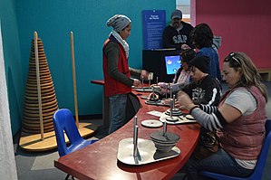 Several people playing with Towers of Hanoi puzzles, with an absolutely enormous 32-disc puzzle behind them.