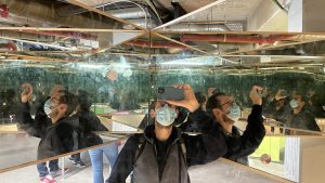 Man enclosed by mirrors taking a picture of his many reflections.