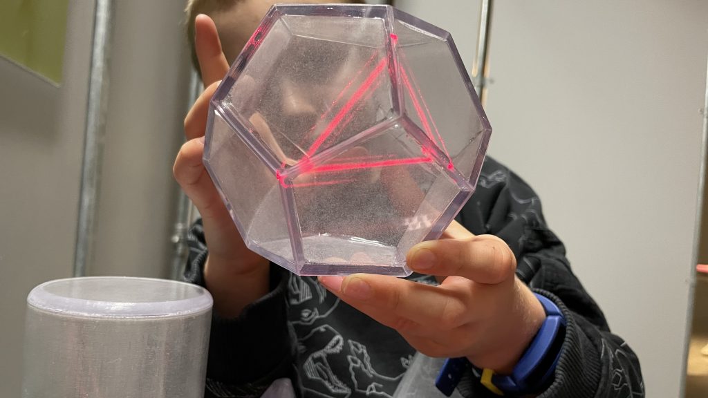 Child holding a transparent dodecahedron through a red light which is showing as a triangle around one vertex