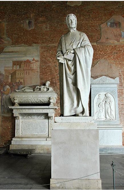 Photograph of a Fibonacci statue. The statue stands on a cuboid of marble and depicts a man in a cape holding a piece of paper.
