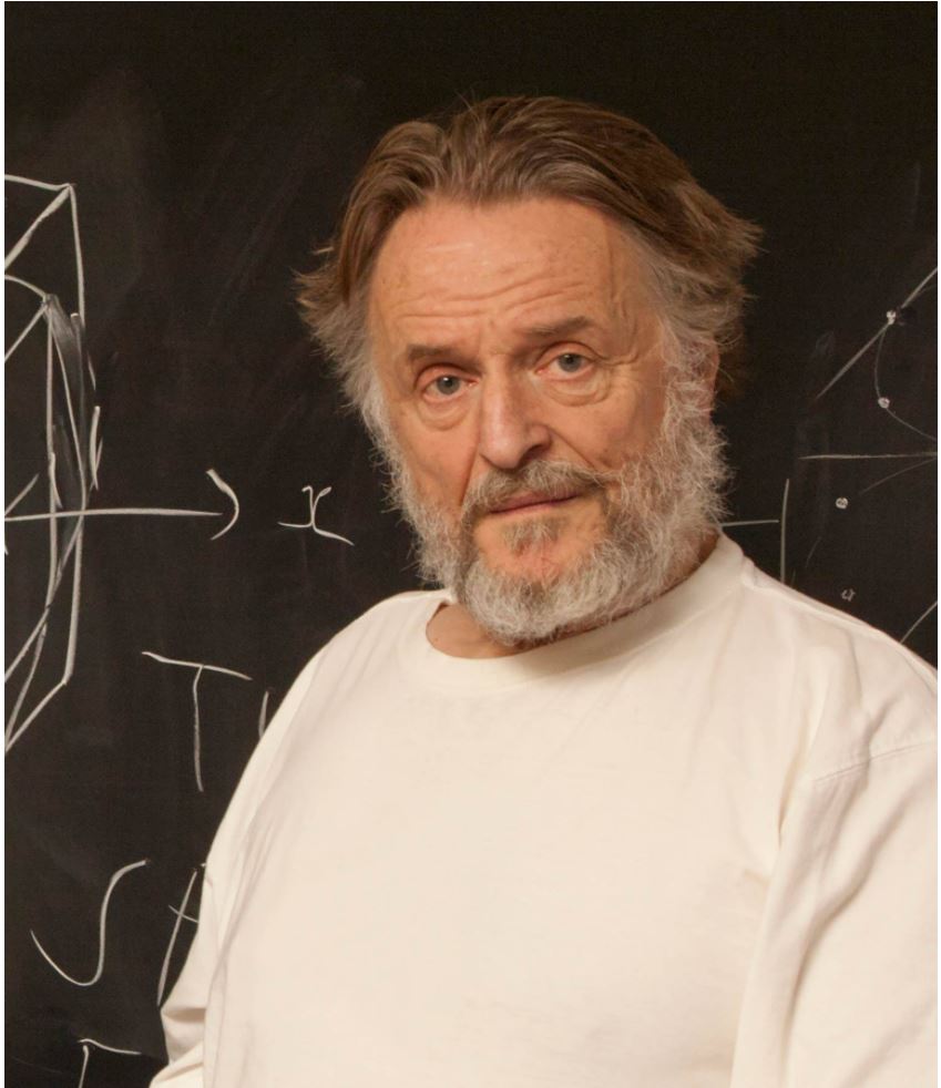 Photo of John Conway standing in front of a blackboard; he is a middle-aged white man with a beard and moustache
