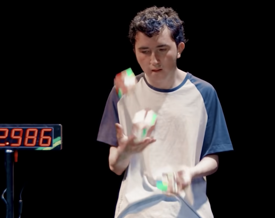 Screenshot from the video, showing a person juggling three partly-solved cubes next to a timer