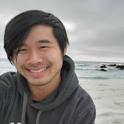 Photo of Howie Hua sitting by the sea. He is a smiling Asian man wearing a grey hoodie