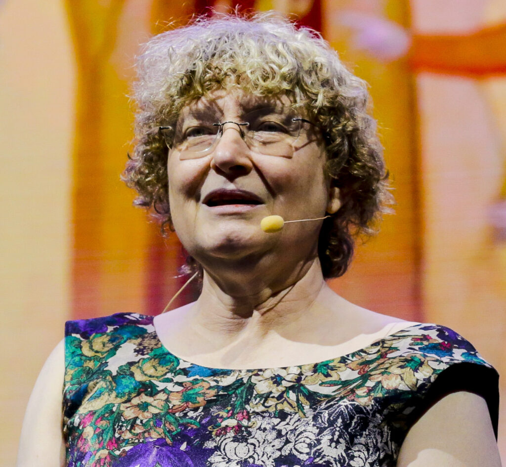 Photo of Ingrid Daubechies, an older white woman with curly blonde hair, speaking on stage with a headset microphone