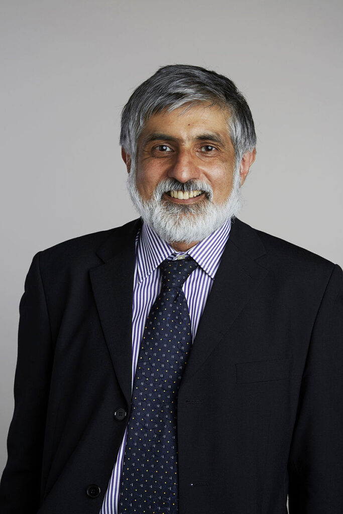 Photo of Philip Kumar Maini, an older man of Indian heritate, with a white beard and grey hair, wearing a suit