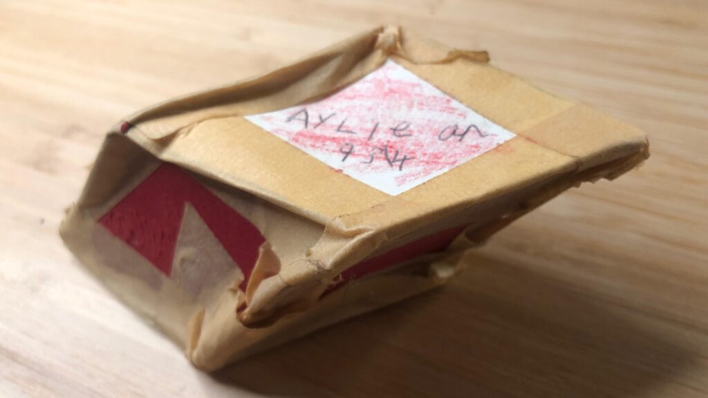 Small battered parallelepiped made of cardboard with "Ayliean 9 3\4" written on it.