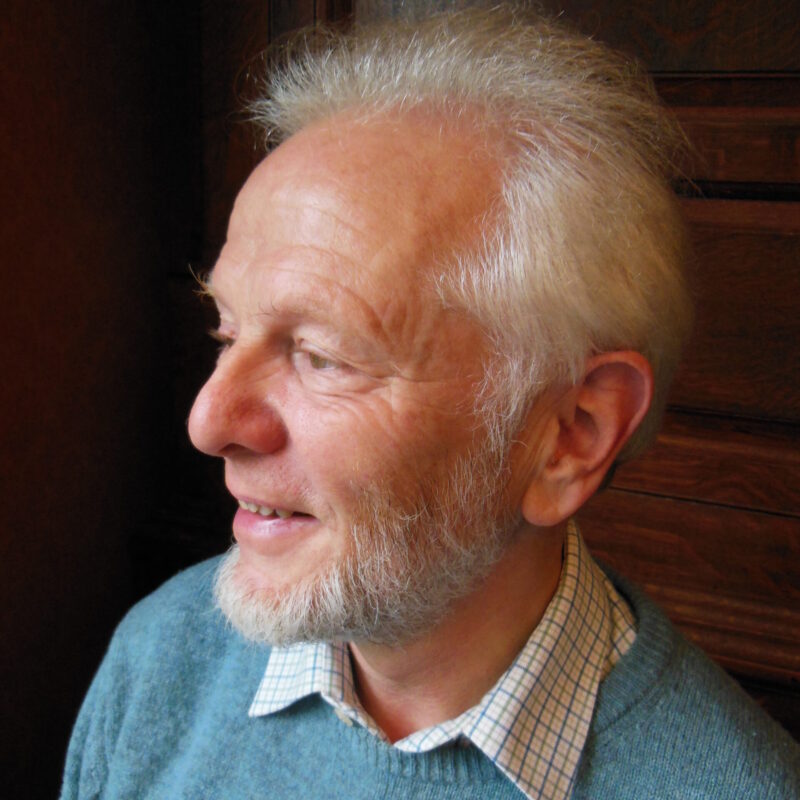 Photo of Jim Simons, an old white man with white hair and a beard, looking to the left in a blue jumper