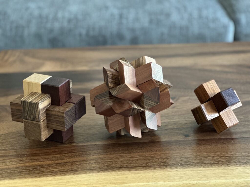 Three 3D wooden puzzles made of interlocking wooden blocks.