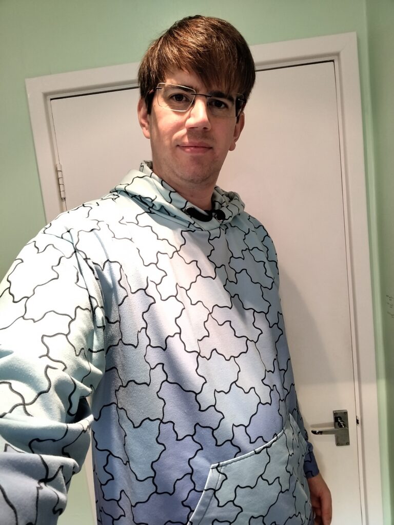 Me wearing a hoodie covered in the Spectre aperioidic monotile.
