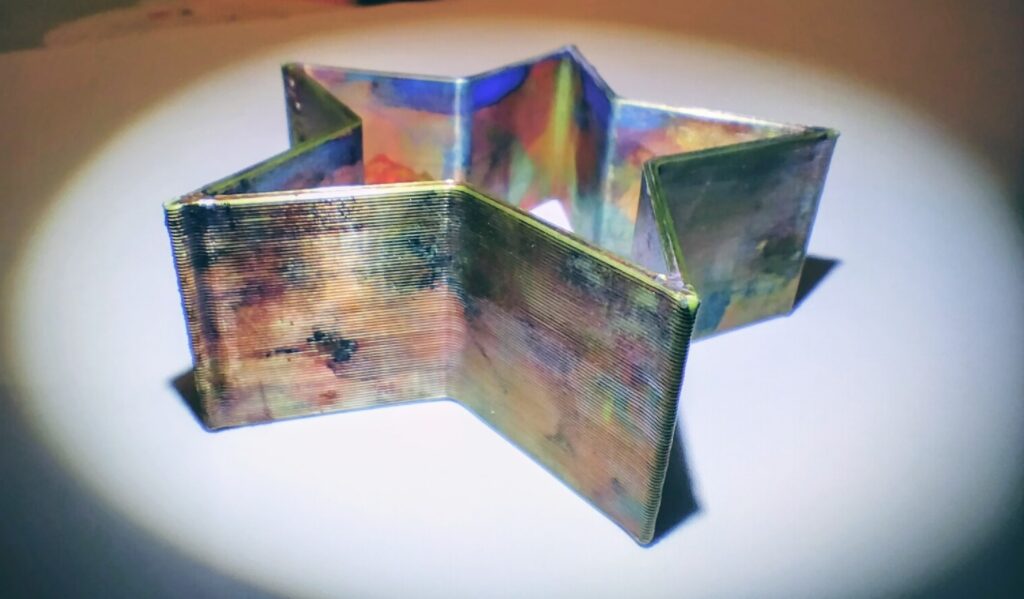 A star-shaped stamper, close up. Splodges of different coloured paints have stained the shiny 3D printed sides.